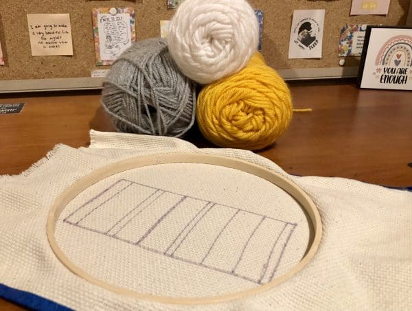 Steps for adorable DIY phone pad made by a punch needle with acrylic yarn.  Punch needle. Punch needle kit. Embroidery Hoop. Monks cloth. Fabric Scissors. Grey, Yellow, and White color scheme. Yarn crafts. Punch needle projects. Phone holder on desk. DIY phone holder.