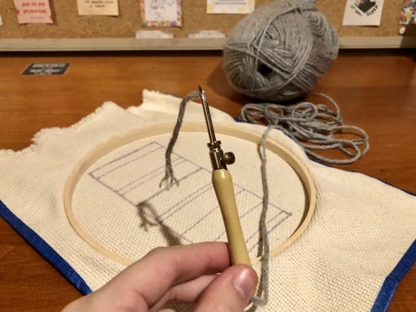 Steps for adorable DIY phone pad made by a punch needle with acrylic yarn.  Punch needle. Punch needle kit. Embroidery Hoop. Monks cloth. Fabric Scissors. Grey, Yellow, and White color scheme. Yarn crafts. Punch needle projects. Phone holder on desk. DIY phone holder.