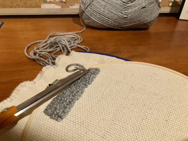 Steps for adorable DIY phone pad made by a punch needle with acrylic yarn.  Punch needle. Punch needle kit. Embroidery Hoop. Monks cloth. Fabric Scissors. Grey, Yellow, and White color scheme. Yarn crafts. Punch needle projects. Phone holder on desk. DIY phone holder.
