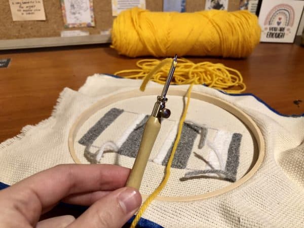 Steps for adorable DIY phone pad made by a punch needle with acrylic yarn.  Punch needle. Punch needle kit. Embroidery Hoop. Monks cloth. Fabric Scissors. Grey, Yellow, and White color scheme. Yarn crafts. Punch needle projects. Phone holder on desk. DIY phone holder.