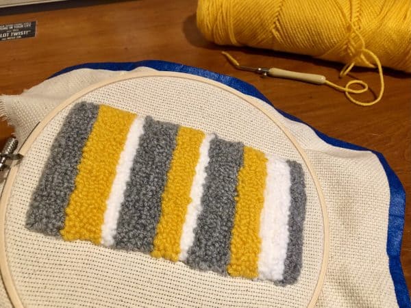 Steps for adorable DIY phone pad made by a punch needle with acrylic yarn.  Punch needle. Punch needle kit. Embroidery Hoop. Monks cloth. Fabric Scissors. Grey, Yellow, and White color scheme. Yarn crafts. Punch needle projects. Phone holder on desk. DIY phone holder.