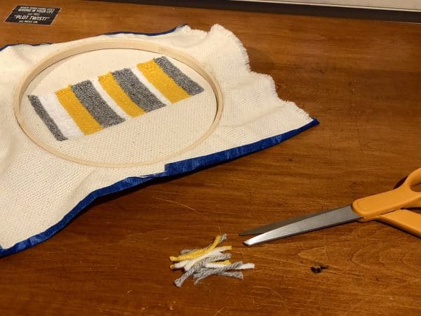 Steps for adorable DIY phone pad made by a punch needle with acrylic yarn.  Punch needle. Punch needle kit. Embroidery Hoop. Monks cloth. Fabric Scissors. Grey, Yellow, and White color scheme. Yarn crafts. Punch needle projects. Phone holder on desk. DIY phone holder.