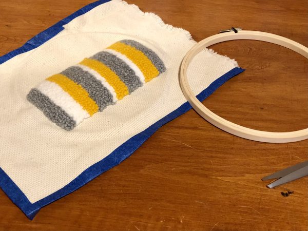 Steps for adorable DIY phone pad made by a punch needle with acrylic yarn.  Punch needle. Punch needle kit. Embroidery Hoop. Monks cloth. Fabric Scissors. Grey, Yellow, and White color scheme. Yarn crafts. Punch needle projects. Phone holder on desk. DIY phone holder.